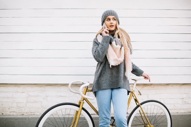 Donna affascinante che comunica sul telefono vicino alla bicicletta