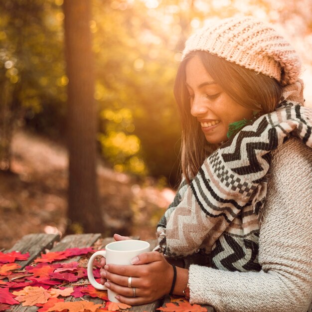Donna affascinante con la tazza una tabella nella sosta di autunno