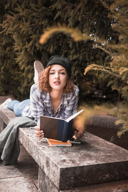 Donna affascinante in cappello nero sulla panca di pietra con il libro