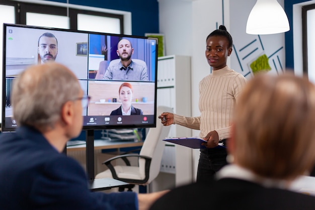 Donna africana che discute con i gestori remoti in videochiamata che presenta nuovi partner in webcam. Gli uomini d'affari che parlano con la webcam, fanno conferenze online partecipano a brainstorming su Internet, ufficio a distanza