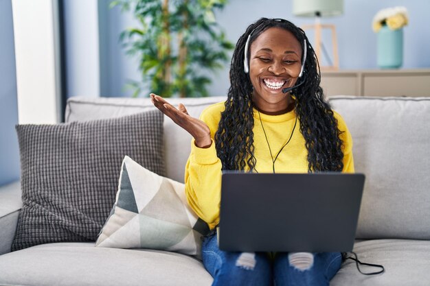 Donna africana che lavora a casa indossando la cuffia dell'operatore che celebra il successo con un sorriso felice e l'espressione del vincitore con la mano alzata