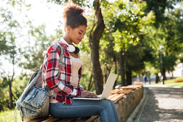 Donna africana che si siede all'aperto nel parco facendo uso del computer portatile.