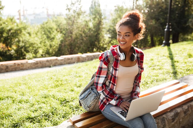 Donna africana che si siede all'aperto nel parco facendo uso del computer portatile.
