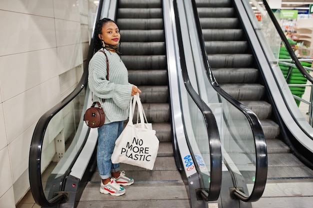 Donna africana con borse ecologiche per lo shopping su scala mobile al centro commerciale