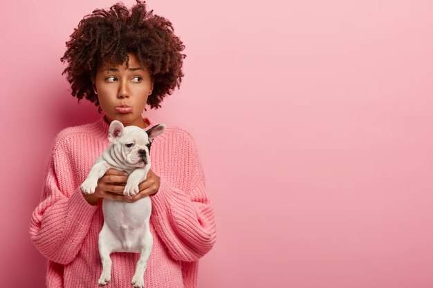 Donna afro-americana che indossa un maglione rosa che tiene cucciolo