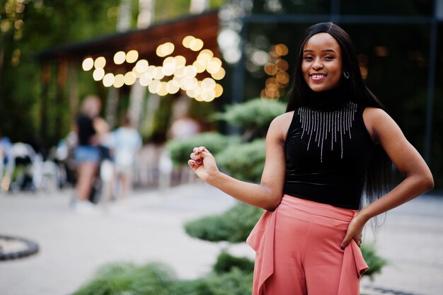 Donna afroamericana alla moda in pantaloni color pesca e camicetta nera posa all'aperto