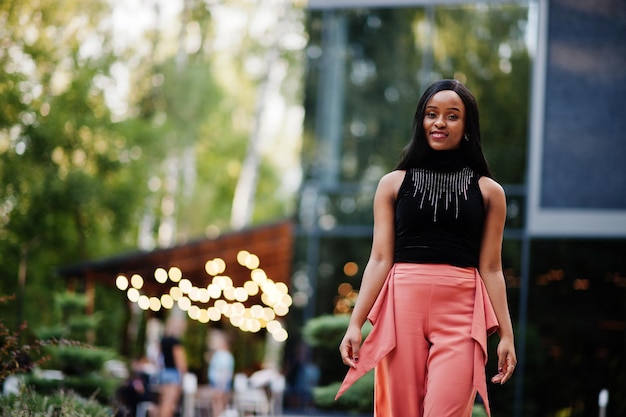 Donna afroamericana alla moda in pantaloni color pesca e camicetta nera posa all'aperto