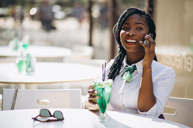 Donna afroamericana con il telefono che beve in un caffè