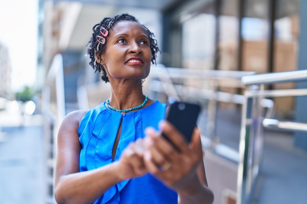 Donna afroamericana di mezza età che sorride fiduciosa utilizzando lo smartphone in strada