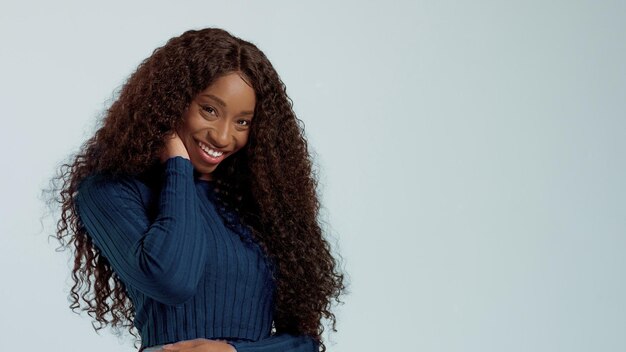 Donna afroamericana di razza mista nera di bellezza con lunghi capelli ricci e un sorriso perfetto che guarda l'obbiettivo e sorride sull'azzurro