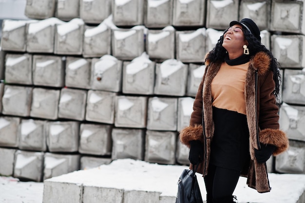 Donna afroamericana in cappotto di pelle di pecora e cappuccio poste al giorno d'inverno su sfondo di pietra innevata