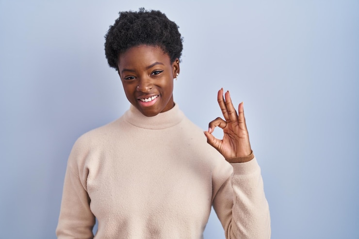 Foto gratuito donna afroamericana in piedi su sfondo blu sorridente positivo facendo segno ok con la mano e le dita espressione di successo