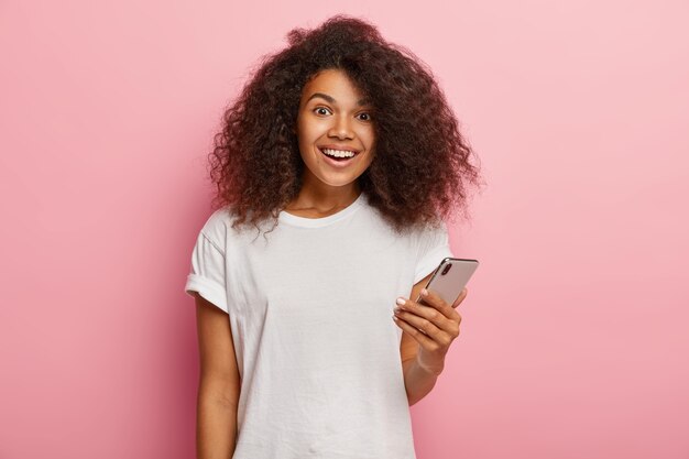 Donna afroamericana soddisfatta in abbigliamento casual, tiene in mano uno smartphone moderno, aspetta una chiamata, felice di ricevere il messaggio dal fidanzato