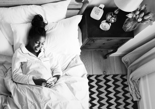 Donna afroamericana sorridente sul letto facendo uso di un cellulare