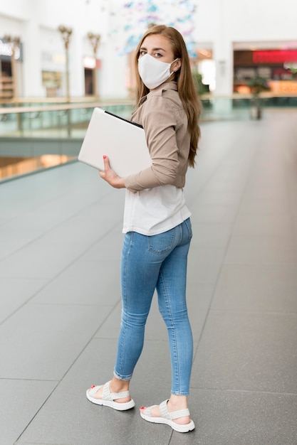 Donna al centro commerciale con la maschera da portare del computer portatile