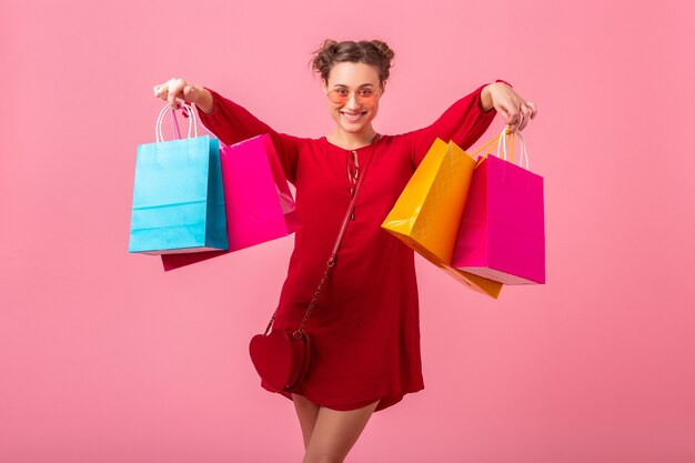 Donna alla moda attraente emozione divertente felice shopping in vestito alla moda rosso che tiene le borse della spesa colorate sul muro rosa isolato, vendita eccitata, tendenza moda primavera estate