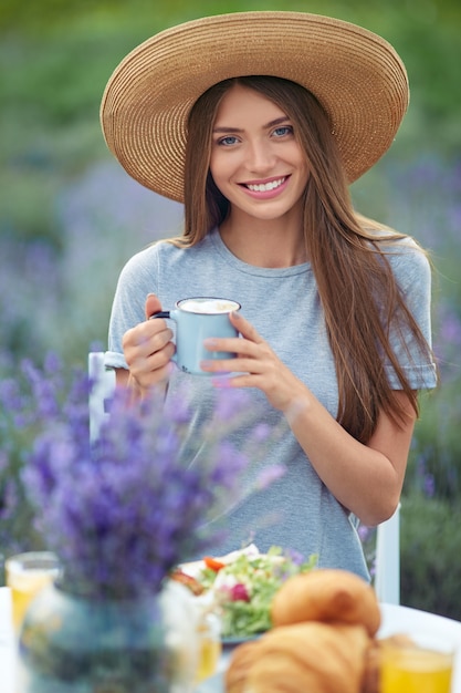 Donna alla moda che gode del caffè nel campo di lavanda