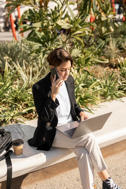 Donna alla moda che lavora al computer portatile all'aperto