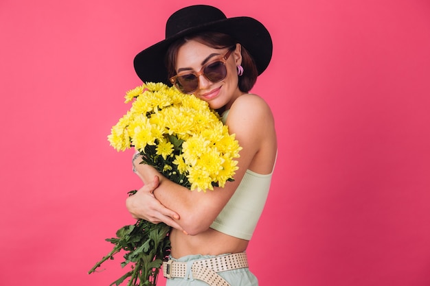 Donna alla moda in cappello e occhiali da sole, abbracciando un grande mazzo di astri gialli, atmosfera primaverile, spazio isolato sorridente calmo