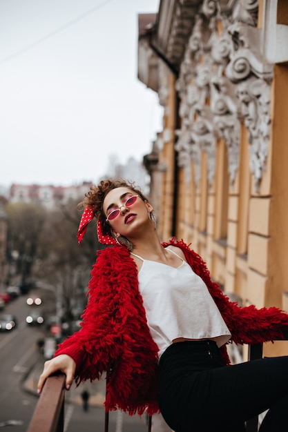 Donna alla moda in occhiali rossi in posa sulla terrazza
