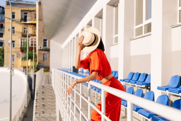 Donna alla moda in vestiti arancioni al tramonto alla posa dello stadio della pista ciclabile