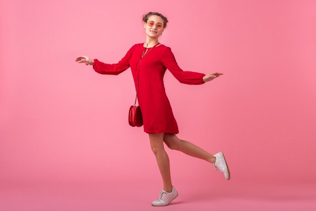 Donna alla moda sorridente felice attraente in vestito alla moda rosso che salta in esecuzione sulla parete rosa isolata, tendenza della moda primavera estate, ragazza innamorata di umore romantico