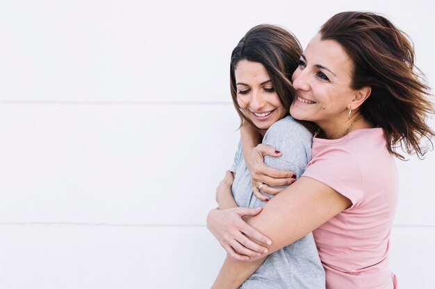 Donna allegra che abbraccia donna vicino al muro bianco