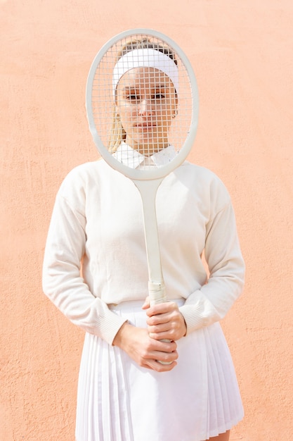 Donna allegra che copre il viso con la racchetta da tennis