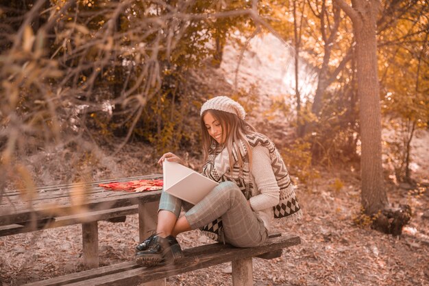 Donna allegra che legge vicino alla tavola nella foresta di autunno