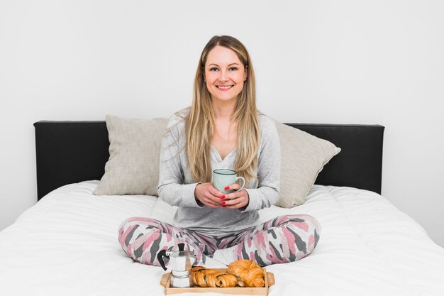 Donna allegra che mangia prima colazione sul letto