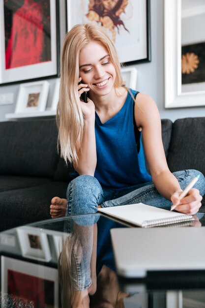 Donna allegra che parla sul telefono cellulare e che scrive in blocco note