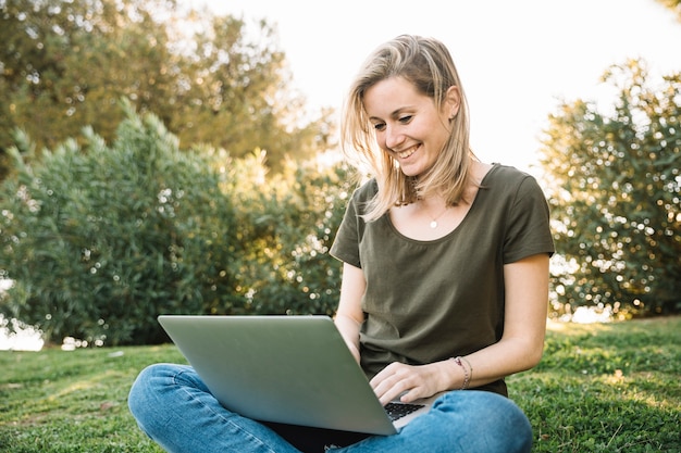 Donna allegra che per mezzo del computer portatile su terra