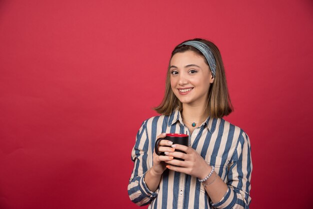 Donna allegra che tiene tazza di caffè e posa davanti