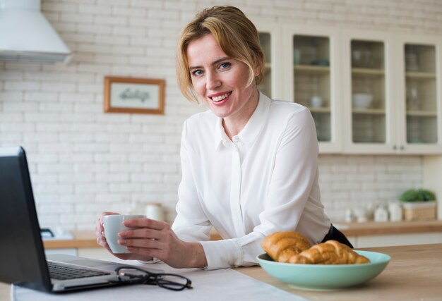 Donna allegra di affari con caffè facendo uso del computer portatile