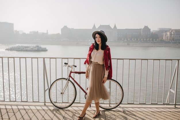 Donna amabile in gonna beige in piedi vicino alla bicicletta