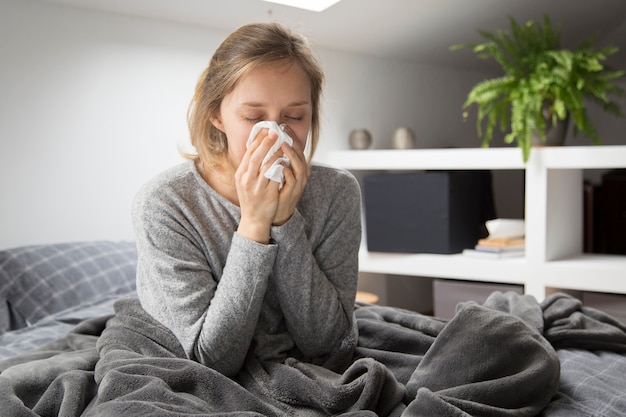 Donna ammalata che si siede a letto, soffiando il naso con il tovagliolo