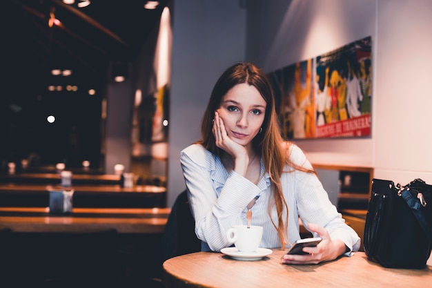 Donna annoiata con lo smartphone che guarda l&#39;obbiettivo