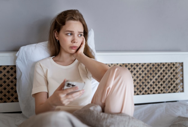Donna ansiosa del colpo medio a letto con lo smartphone