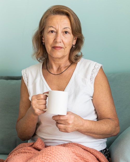 Donna anziana a casa durante la pandemia gustando una tazza di caffè