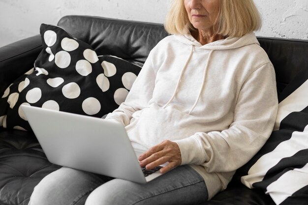 Donna anziana a casa sul divano che lavora al computer portatile