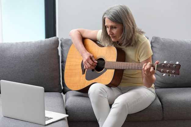 Donna anziana a casa sul divano che usa il laptop per lezioni di chitarra