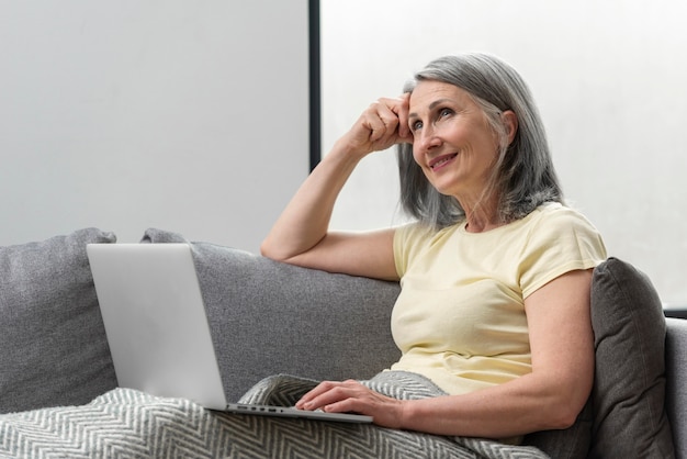 Donna anziana a casa sul divano usando il laptop