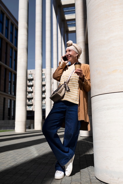 Donna anziana all'aperto in città parlando al telefono mentre beve caffè