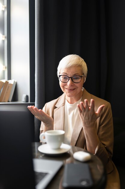 Donna anziana che beve caffè in un bar mentre guarda il suo laptop