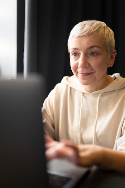 Donna anziana che beve caffè in un bar mentre lavora al suo laptop