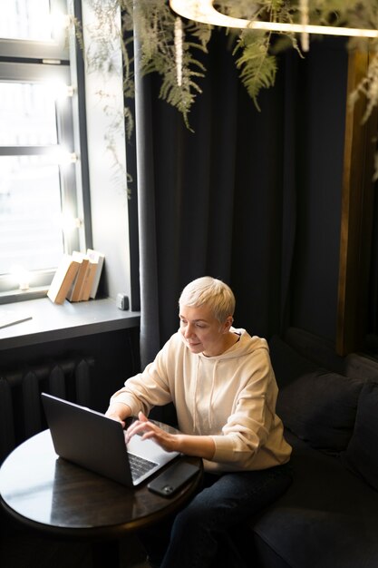 Donna anziana che beve caffè in un bar mentre lavora al suo laptop