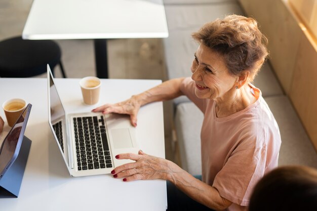 Donna anziana che lavora al suo laptop e trascorre del tempo con gli amici