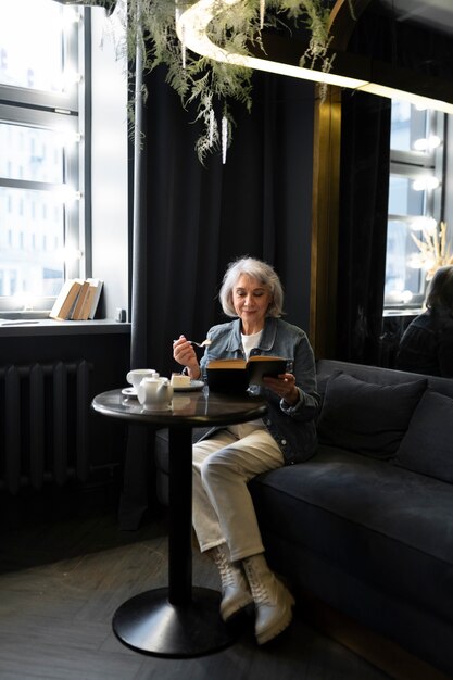 Donna anziana che legge un libro e beve caffè in un bar