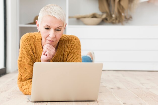 Donna anziana che pensa e che esamina computer portatile