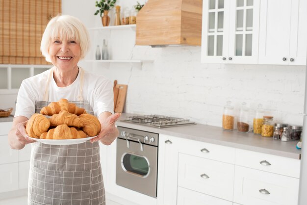 Donna anziana che tiene un piatto con i croissant